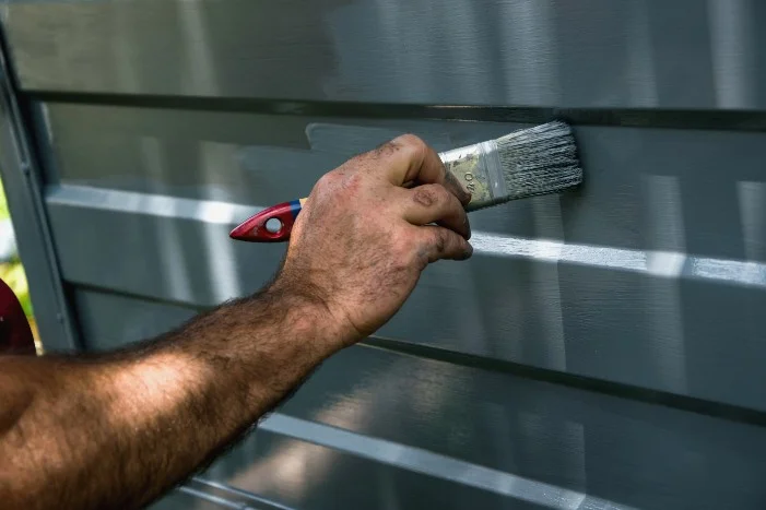 Person streicht Holzfassade mit Pinsel
